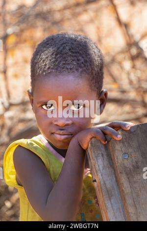 portrait d'un enfant africain dans la cour, la vie du village, la fille tient une chaise en bois Banque D'Images