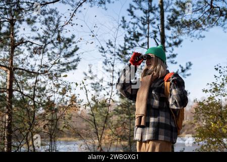 Observateur d'oiseaux touristique de femme concentrée dans la forêt d'automne regardant à travers des jumelles sur les oiseaux. Tourisme. Banque D'Images