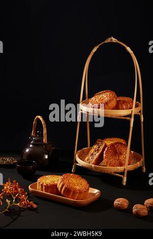 Panier en bambou à deux niveaux avec quelques délicieux gâteaux de lune décorés sur fond noir. Lanternes chinoises et pleine lune sur la rivière nocturne pour le milieu-autum Banque D'Images
