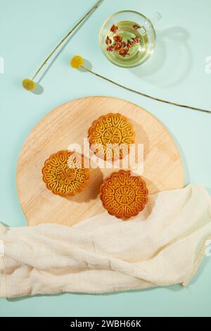 Trois mooncakes placés sur une planche à découper en bois avec une serviette blanche. Tasse transparente remplie de thé chaud et de fleurs séchées. Concept de Mooncake sur Mid Banque D'Images