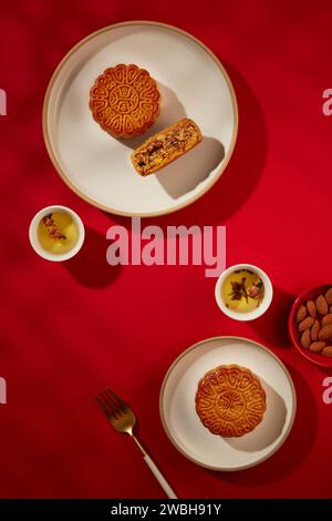 Vue de dessus de quelques gâteaux de lune placés sur des assiettes blanches, deux tasses de thé, une fourchette et un plat de noix d'amande. Les Chinois ont eu la coutume de wat Banque D'Images