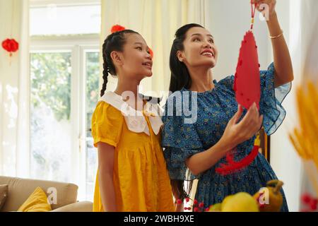 Fille excitée regardant la mère accrocher des décorations Têt sur les murs de la maison Banque D'Images