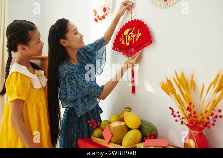 Mère joyeuse et fille adolescente accrochant des décorations traditionnelles de festival de printemps sur les murs de l'appartement Banque D'Images