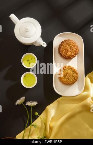 Un ensemble de thé décoré de deux délicieux gâteaux de lune placés sur un plat en céramique. Tissu jaune avec des fleurs en vedette. Fête de la mi-automne traditi chinois Banque D'Images