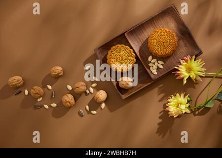 Plats anciens en bois avec de savoureux gâteaux de lune placés dessus. Les noix, les graines de tournesol et les graines de citrouille sont éparpillées sur fond brun avec des fleurs. HAP Banque D'Images