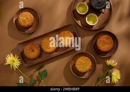 Un ensemble de thé de couleur noire et plusieurs savoureux gâteaux de lune sont disposés sur des plats ronds et rectangulaires. Fond marron. Fond nourriture et boisson thé an Banque D'Images