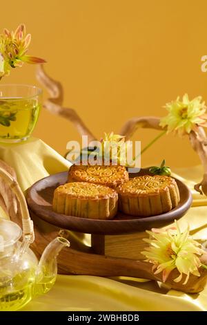 Vue de face du dessert du festival chinois sur une assiette en tissu jaune, décorée de fleurs et de branches d'arbres. Un service à thé transparent en vedette. St minimaliste Banque D'Images