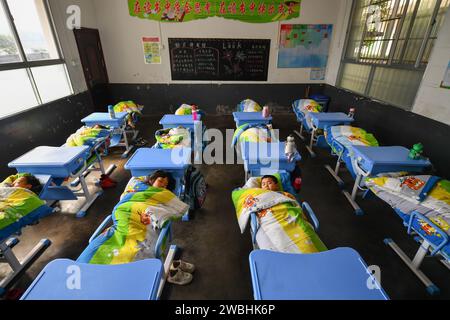 Changsha, province chinoise du Hunan. 10 janvier 2024. Les élèves de première année font une sieste pendant la pause de midi sur des chaises pliables dans une école primaire de la ville de Liuyang, dans la province du Hunan, au centre de la Chine, le 10 janvier 2024. Un lot de chaises pliantes a été mis en service dans les salles de classe d'une école primaire dans la ville de Longfu de la ville de Liuyang. Les chaises, qui peuvent être posées lorsque les élèves doivent faire une sieste à midi, peuvent grandement améliorer la qualité du sommeil des élèves. Crédit : Chen Zeguo/Xinhua/Alamy Live News Banque D'Images