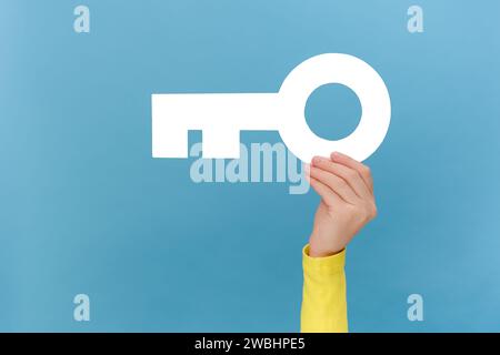 Gros plan de la main de femme tenant la clé de papier blanc, la propriété, le loyer et le concept immobilier, posant isolé sur le mur de fond de couleur bleue unie dans l'esprit de studio Banque D'Images