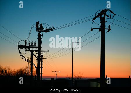 Poteaux électriques avec lignes électriques au coucher du soleil. Transport d'électricité. Piliers en béton avec isolateur de contrainte. Câbles électriques suspendus. Banque D'Images