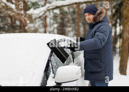 jeune homme enlevant la neige de sa voiture avec la brosse. concentrez-vous sur le pinceau Banque D'Images