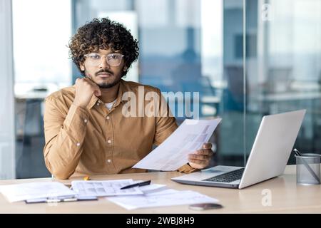 Portrait d'homme d'affaires concentré sérieux à l'intérieur du bureau, homme regardant la caméra tenant des documents rapports financiers, comptable financier avec ordinateur portable sur le travail de papier. Banque D'Images