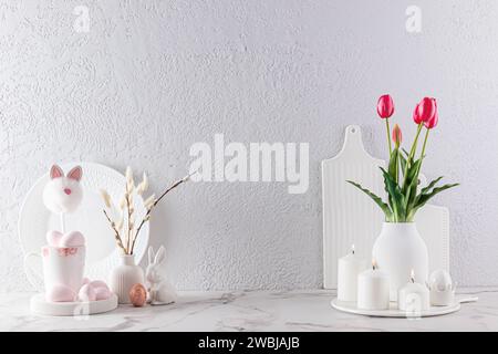 Fond de cuisine dans des couleurs claires pour les vacances de Pâques. Fleurs et saules dans des vases, bougies, œufs de Pâques et lapins sur un comptoir en marbre Banque D'Images