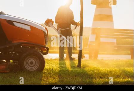 Jardinier tond la pelouse tôt le matin à l'aube. Entretien des pelouses. Banque D'Images