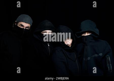 photo de studio de quatre personnes portant des vêtements noirs avec des visages cachés sur le fond noir Banque D'Images