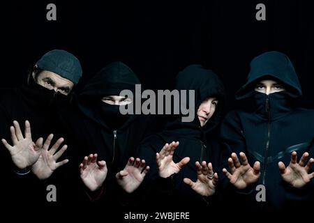 photo de studio de quatre personnes portant des vêtements noirs avec des visages cachés sur le fond noir tenant leurs paumes vers le haut Banque D'Images