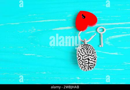 Vue de dessus d'un modèle miniature de cerveau humain et d'un cadenas ouvert en forme de coeur rouge complet avec une clé maîtresse isolée sur fond en bois bleu avec copie Banque D'Images