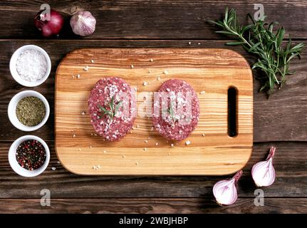 Côtelettes rondes de viande crue - pour cuisiner des hamburgers faits maison. Côtelettes sur une planche à découper en bois. Pose à plat. Vue de dessus. Plan de travail en bois. Banque D'Images