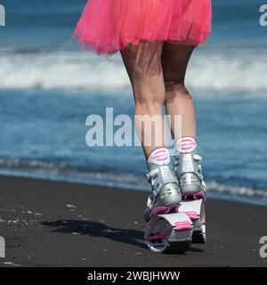 Jambes de femme sportive vue arrière en Kangoo Jumps bottes de sport et jupe rose courte courant sur la plage pendant l'exercice aérobie en plein air. Section basse Banque D'Images
