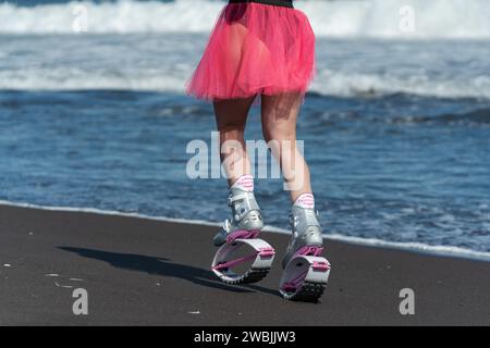 Jambes de femme sportive en Kangoo Jumps bottes de sport, maillot de bain noir et jupe courte courir et sauter sur la plage pendant Banque D'Images