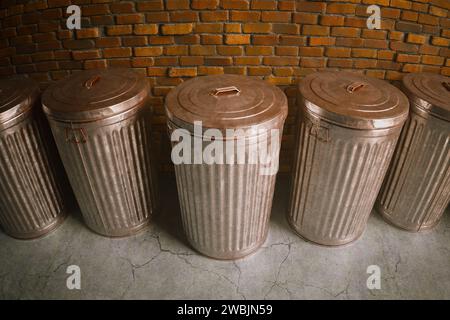 Un éventail de poubelles métalliques de style vintage avec des couvercles ajustés est méthodiquement positionné sur le fond d'un mur de briques rouges patiné, exsudant Banque D'Images