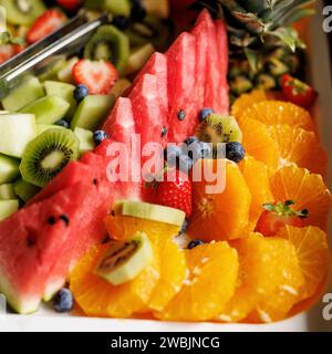 Un plateau de fruits vibrant avec de la pastèque, du kiwi, des fraises, des myrtilles et des oranges sur un plat blanc. Banque D'Images