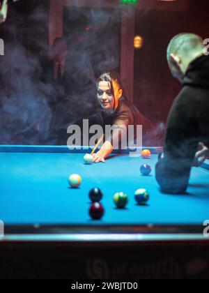 Jeune femme jouant au billard alignés pour tirer un coup gagnant Banque D'Images