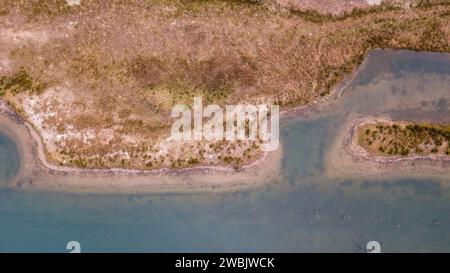 Il s'agit d'une prise de vue aérienne capturant les courbes complexes d'un rivage serpentin où la terre rencontre l'eau. La juxtaposition du terrain accidenté et végétalisé contre les eaux bleues placides crée une peinture abstraite naturelle. Le rivage est découpé avec de nombreuses petites criques et promontoires, suggérant un paysage dynamique façonné par les courants d'eau et peut-être la faune locale. La végétation semble résistante à la sécheresse, typique d'une région semi-aride. L'image évoque les thèmes des modèles naturels, des écosystèmes de bord d'eau et du délicat équilibre entre la terre et l'eau. Serpentin Shoreline Aerial V Banque D'Images