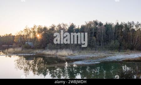 Cette image capture la beauté tranquille d'un lac au crépuscule. Le soleil couchant projette une lueur douce et chaude sur la scène, tandis que le bleu frais de la nuit imminente commence à se coucher. La surface vitreuse du lac reflète la forêt environnante et les couleurs pastel du ciel, créant un équilibre symétrique entre la terre et l'eau. Le paysage est dépourvu d'activité humaine, ce qui permet au calme de la nature d'être le point focal. Serein Lakeside au crépuscule. Photo de haute qualité Banque D'Images