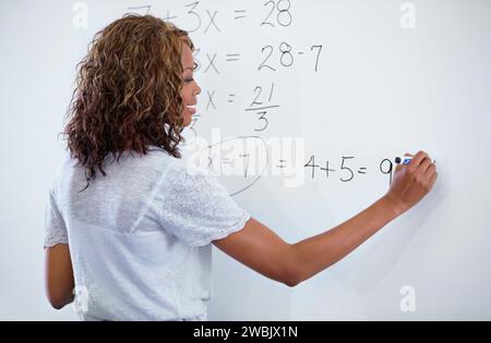 Femme, enseignante et écriture sur tableau blanc pour les maths, les nombres ou les équations en classe. Vue arrière d'une personne féminine, d'un éducateur ou d'un conférencier avec somme activée Banque D'Images