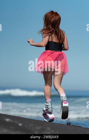 KAMCHATKA, RUSSIE - 15 JUIN 2022 : vue arrière de la femme sportive en Kangoo Jumps bottes de sport, maillot de bain noir une seule pièce et jupe rose courte saut et Banque D'Images