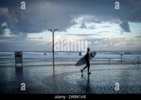 Tel Aviv, Israël. 11 janvier 2024. Un passant porte sa planche de surf le long de la promenade méditerranéenne tôt le matin. Crédit : Kay Nietfeld/dpa/Alamy Live News Banque D'Images