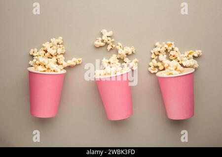 Pop-corn dans des tasses roses. Trois tasses de pop-corn sur fond gris. Pop-corn sucré. Vue de dessus Banque D'Images