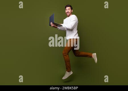 Photo pleine longueur de l'homme gentil joyeux habillé des vêtements élégants courant le bureau pressé isolé sur fond de couleur kaki Banque D'Images