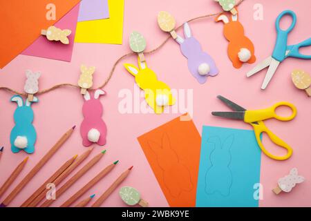 Lapins de Pâques faits à la main à partir de papier coloré, artisanat facile pour les enfants sur fond rose. Vue de dessus. Banque D'Images