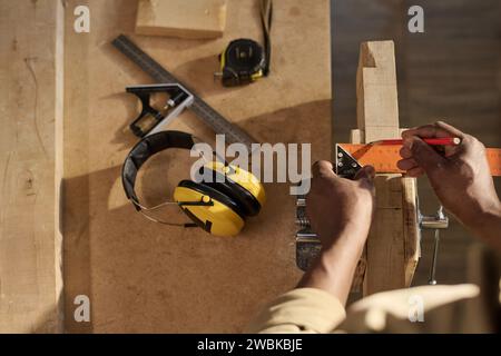 Gros plan de menuisier méconnaissable mesurant le bois et les meubles de construction au poste de travail à la lumière du soleil Banque D'Images