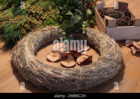 Une couronne vierge, des pommes de pin et de la verdure de sapin reposent sur une table. Les ustensiles sont utilisés pour créer une couronne de l'Avent auto-liée. Banque D'Images