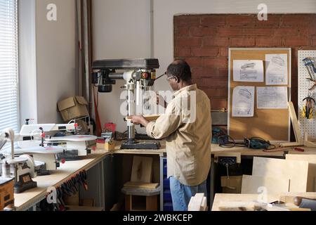 Vue arrière de l'homme afro-américain senior coupant le bois à l'aide de machines dans l'atelier de charpentiers Banque D'Images