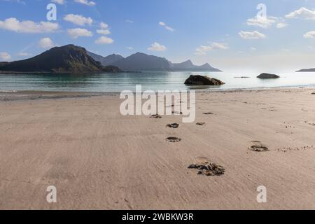 Traces de pas vers la mer sur Haukland Beach, Lofoten, Norvège, avec des îlots rocheux et des montagnes brumeuses sous une douce lumière du matin, mise au point sélective Banque D'Images