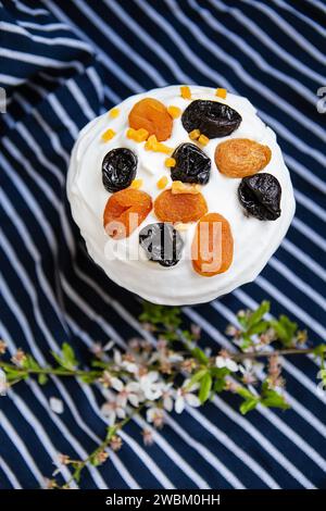 Le gâteau de Pâques, décoré d'abricots et de pruneaux séchés, se dresse sur un tablier bleu rayé, une branche fleurie. Concept de vacances religieuses de Pâques Banque D'Images