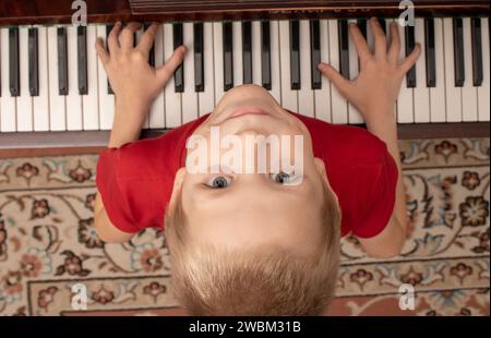 Jeune garçon assis au piano à la maison. Le garçon tient ses mains sur les clés et lève les yeux Banque D'Images