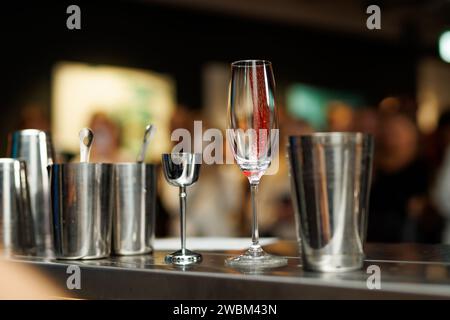 Un comptoir en bois avec une flûte à champagne et des outils de bar en argent au premier plan et une vue floue d'une foule de fête en arrière-plan Banque D'Images