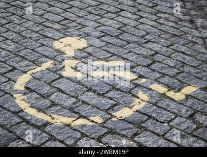Symbole handicapé jaune délavé peint sur une surface pavée Banque D'Images
