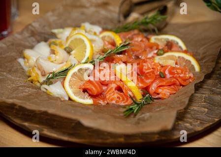 Un plateau de fruits de mer délicatement arrangé composé de saumon fumé, de tranches de citron et d'herbes fraîches, servi sur parchemin pour une entrée gastronomique. Banque D'Images