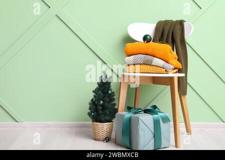 Vêtements empilés sur la chaise avec boîte-cadeau et petit arbre de Noël près du mur en bois vert Banque D'Images