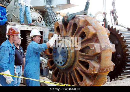 CENTRE SPATIAL KENNEDY, FLA. - Un ouvrier graisse le pignon géant qui sera installé sur le Crawler-transporter (fond). Le pignon d'entraînement fait tourner le tapis sur le CT. Le pignon est couplé à l'engrenage qui se fixe au moteur d'entraînement. Le CT se déplace sur huit bandes de roulement à chenilles, chacune contenant 57 patins de bande de roulement, pour un poids combiné de 957 600 livres. Le CT transporte la navette spatiale au-dessus de sa plate-forme de lancement mobile, ajoutant 12 millions de livres supplémentaires, du bâtiment d'assemblage des véhicules à la plate-forme de lancement. NASA et United Space Alliance (USA) ingénieurs de systèmes CT et techniciens américains ar Banque D'Images