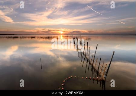 Photographie d'un paysage avec des filets de pêcheurs et des cannes dans l'eau lors d'un coucher de soleil sur le lac de l'Albufera avec un reflet parfait, à Valence, Espagne Banque D'Images