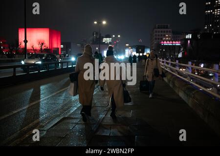 Les navetteurs rentrent chez eux une nuit d'hiver à travers Waterloo Bridge à côté d'un théâtre national rouge illuminé bankside, Southbank, centre de Londres, Angleterre. Banque D'Images