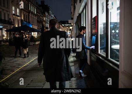 Un homme effectue un retrait d'argent d'un distributeur de billets par une nuit d'hiver sombre dans le quartier de Covent Garden dans le West End de Londres, en Angleterre, au Royaume-Uni Banque D'Images