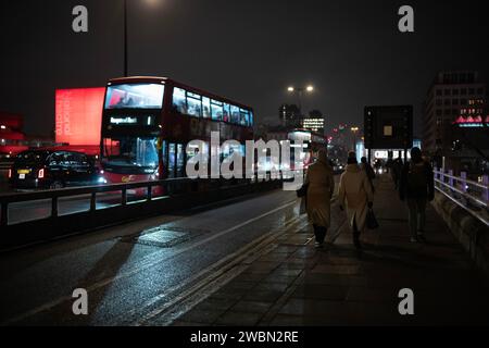 Les navetteurs rentrent chez eux une nuit d'hiver à travers Waterloo Bridge à côté d'un théâtre national rouge illuminé bankside, Southbank, centre de Londres, Angleterre. Banque D'Images